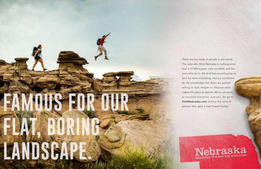 a magazine spread with people walking on top of a rock formation and the words "Famous for our flat, boring, landscape" imposed on top. To the right, ad copy is too small to read and the Nebraska logo is underneath