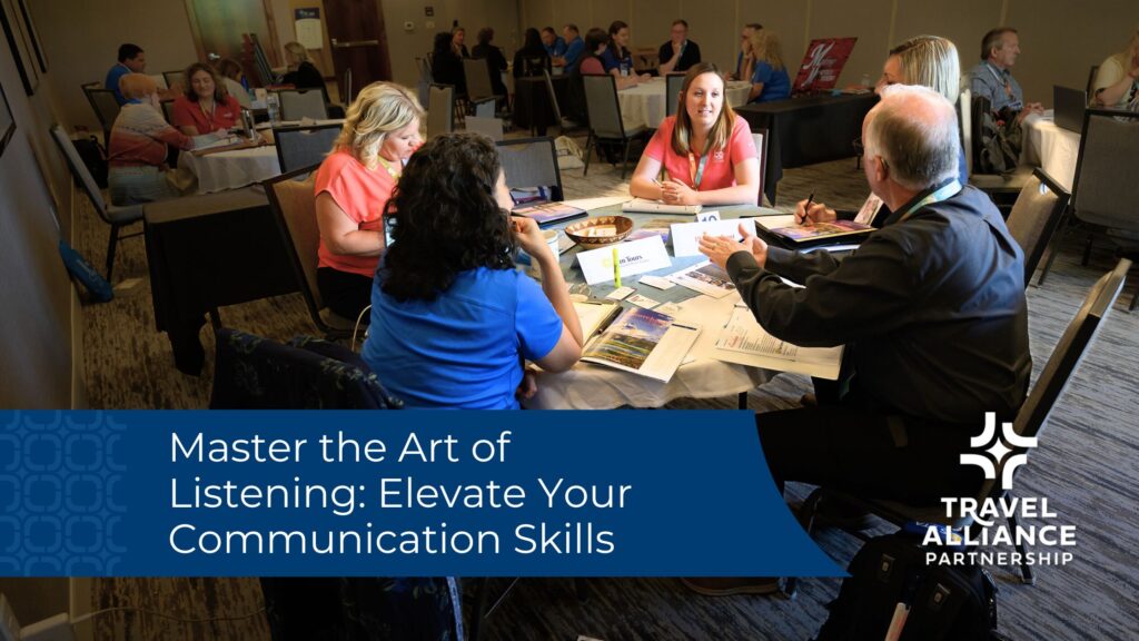 A long conference room with round tables, people are seated at all the tables. In the foreground, a table of five people talks, with papers spread out around the table. A blue banner imposed on the image reads "Master the art of listening: elevate your communication skills"